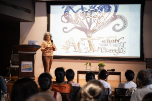 photo of Andrea Kantrowitz in front of a projected image of her work as she speaks to the audience